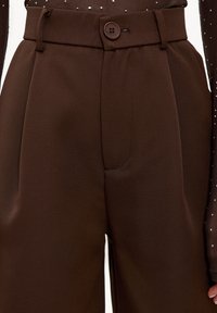 Pantalon marron à jambes larges en tissu lisse, doté d'une fermeture à boutons sur le devant, de plis et de poches latérales pour plus de fonctionnalité.