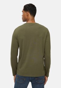 Olijfgroene longsleeve t-shirt van zachte stof, met een ronde halslijn en een comfortabele pasvorm, gecombineerd met blauwe spijkerbroeken.