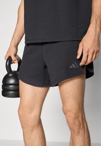 Shorts de sport noirs avec une texture lisse et un design à fente sur le côté. Présente un petit logo adidas foncé sur le bord inférieur.
