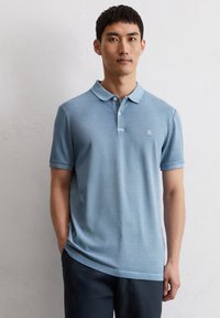 Lichtblauwe poloshirt met kraag, korte mouwen en een voorpanneel met twee knopen. Subtiele textuur en klein logo op de borst.