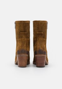 Botas de tobillo de ante marrón con un tacón de madera apilada, que cuentan con un cierre lateral de cremallera y una pestaña trasera en bucle para un fácil calzado.