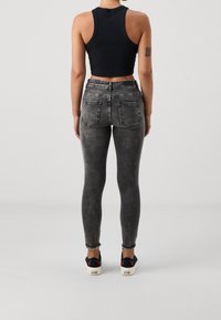 Top corto negro combinado con jeans ajustados negros deslavados. Los pantalones tienen bolsillos traseros y un dobladillo deshilachado, junto con zapatillas negras.