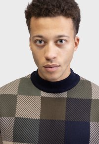 Pull en tricot avec un col haut en côtes bleu marine. Décoré de grands blocs en olive, crème et bleu marine, avec des rayures diagonales.