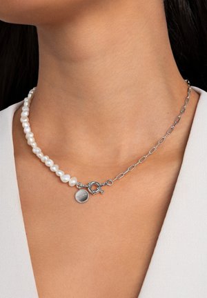 Perlenkette mit unregelmäßig geformten weißen Perlen, einer silbernen Kette und einem runden metallischen Verschluss mit dekorativem Element.