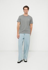 Szürke pamut rövid ujjú póló kerek nyakkivágással, világoskék bő fazonú farmerral és fekete cipővel, fehér részletekkel párosítva.