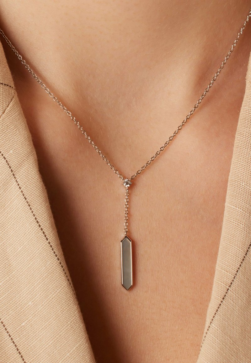 Collier en argent avec un pendentif rectangulaire présentant une surface lisse et réfléchissante, suspendu à une délicate chaîne en perles.