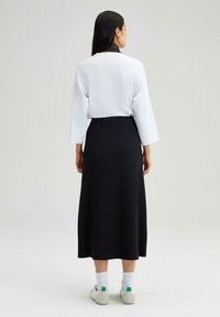 Vit oversized topp med rund halsringning, i kombination med en svart midikjol. Lätt tyg, avslappnad passform, och ankellåga sneakers med gröna accenter.