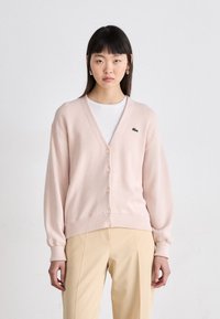 Cardigan rosa claro feito de tecido macio, com decote em V, fecho com botões, punhos canelados e pequeno logotipo verde no peito.