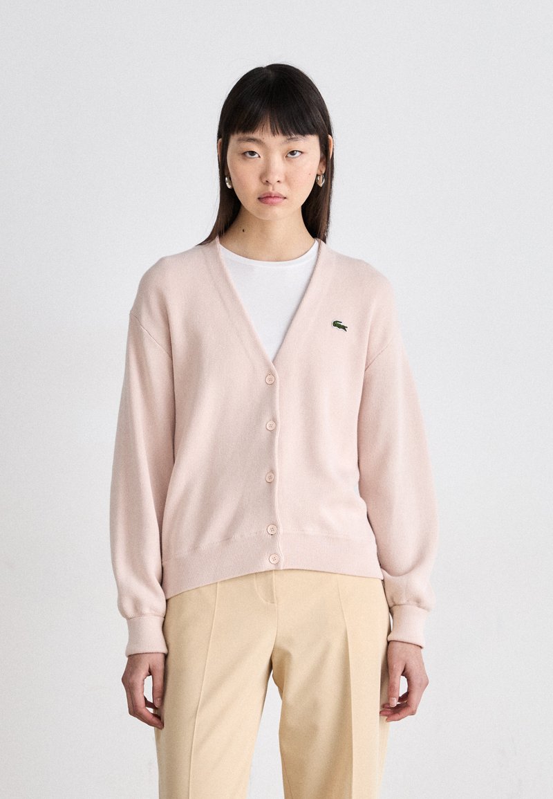 Cardigan rosa claro feito de tecido macio, com decote em V, fecho com botões, punhos canelados e pequeno logotipo verde no peito.