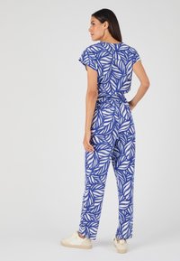 Combinaison bleu avec motif de feuilles blanches ; manches courtes, taille élastique et design droit ; associée à des baskets légères.