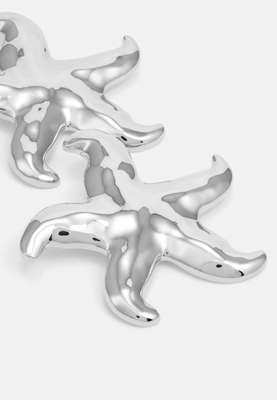 Oggetto decorativo a forma di stella marina argentata con una superficie liscia e lucida, caratterizzato da cinque braccia appuntite e un design solido e riflettente.