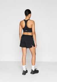 Top deportivo atlético negro y pantalones cortos, con un diseño de espalda racer, cinturilla elástica y detalles reflectantes. Zapatillas negras y calcetines blancos.