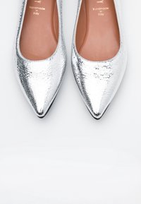 Stříbrné ploché baleríny s špičatou špičkou vyrobené z texturované kůže s lesklým povrchem, s nahým stélkou a vyraženým detailem "Ruční výroba v Itálii".