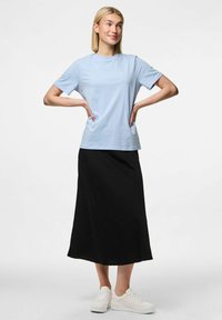 T-shirt azul claro de manga curta combinado com uma saia preta até o tornozelo. A modelo usa ténis brancos, com os braços colocados na cintura.