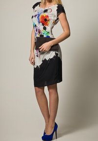 Figurnära klänning med färgglada abstrakta mönster på en vit överdel, som övergår till en enfärgad svart nederdel. Bärs med en svart kuvertväska och blå klackar.