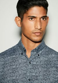 Camicia a maniche corte con bottoni di colore blu navy, decorata con un intricato motivo floreale, dotata di colletto a punte e bottoni neri.