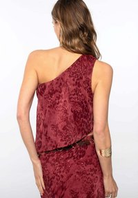 Haut sans manches bordeaux avec un design asymétrique et un imprimé léopard ; comporte un accent de ceinture circulaire métallique à la taille et un tissu texturé.