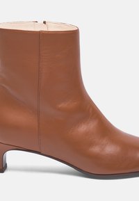 Bottine en cuir marron avec une texture lisse, petit talon carré et un design minimaliste, dotée d'une fermeture éclair sur le côté.