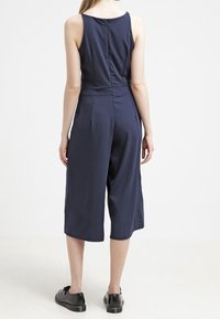 Mono azul marino con un diseño sin mangas, piernas anchas cortas y cremallera en la espalda. Fabricado con una tela suave y un ajuste entallado.