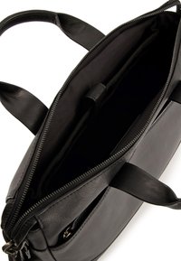 Schwarze Ledertasche mit einem Reißverschluss und zwei Griffen. Das Innere verfügt über eine Stoffauskleidung mit Fächern zur Organisation und einem eleganten, klaren Design.