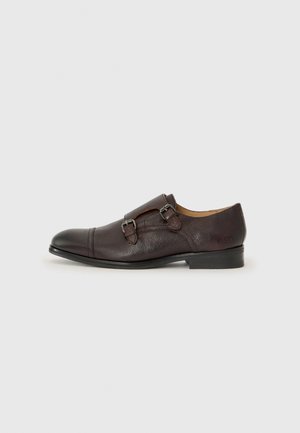 Zapato de vestir de cuero marrón con dos hebillas, punta redondeada y parte superior texturizada. Diseño formal con un tacón bajo y un acabado suave.