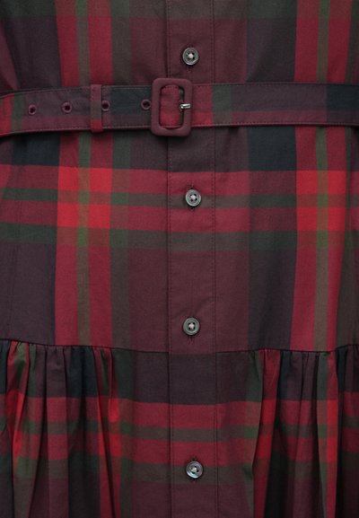 Sarkana un zaļa rūtainā kleita ar pogu priekšpusi, jostasvietu un izpletni svārku daļu. Komplektā atbilstoša josta un melnas pogas. Izgatavota no mīksta kokvilnas materiāla.