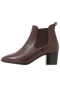 Bottine en cuir marron à bout pointu, avec des panneaux latéraux élastiques et un talon carré empilé. La semelle noire texturée ajoute de la stabilité.