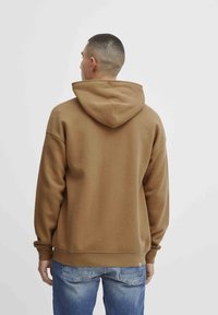 Sweatshirt à capuche marron avec une coupe décontractée, doté d'une poche kangourou et de poignets côtelés. Un jean en denim bleu complète le look.