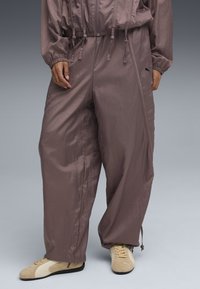 Pantalons de coupe-vent violets avec taille réglable à cordon, texture élégante et zips sur les côtés, assortis à des chaussures beiges.