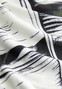Tissu avec une base blanche, des motifs abstraits noirs et des accents verts, présentant une texture lisse et un drapé doux.