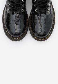 Błyszczące czarne buty za kostkę z koronką w fakturze krokodyla oraz wyraźnym żółtym przeszyciem wzdłuż krawędzi podeszwy na białym tle.