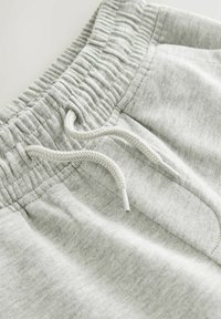 Pantalons de survêtement gris clair avec une taille côtelée, un cordon de serrage et une texture en coton doux, dotés de poches latérales et de détails de couture minimaux.