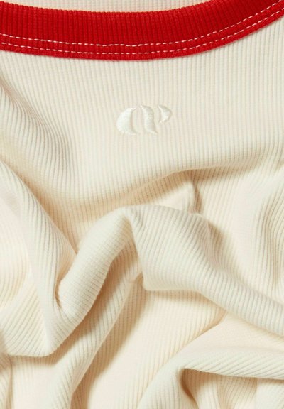 Tessuto a coste crema con colletto rosso e accenti bianchi ricamati; presenta un logo ricamato in una texture morbida.