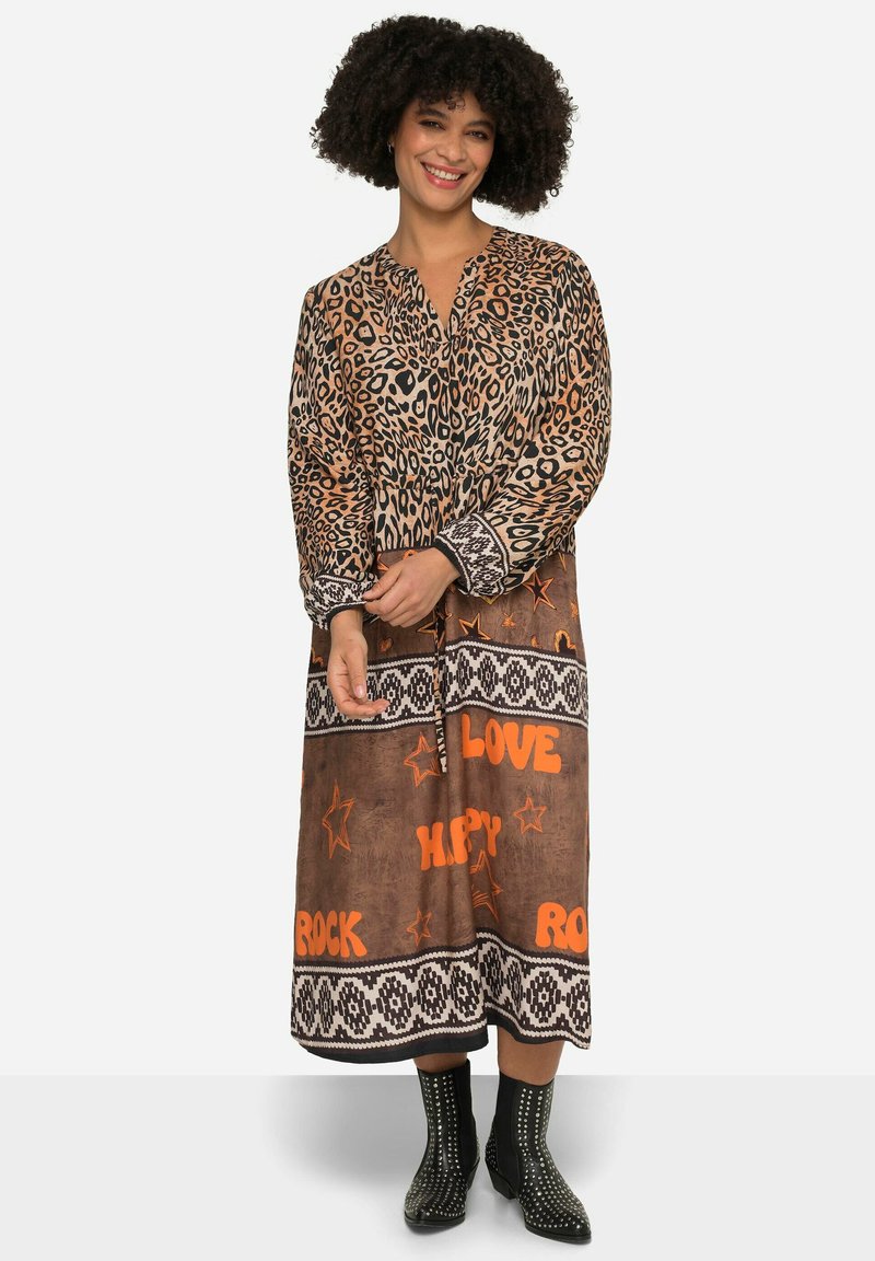 Robe à imprimé léopard dans des tons terreux avec un col, des manches longues et un texte décoratif orange. Des bottines noires à clous complètent la tenue.