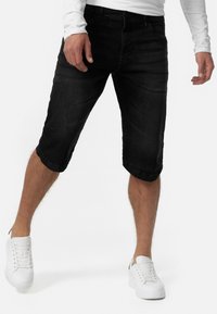 Crne traperice s ravnim nogavicama, srolanim rubovima, petljama za remen i prednjim džepovima; nosi se s bijelim tenisicama i majicom dugih rukava.