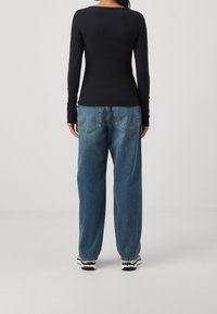 Sort langærmet skjorte og blå højtaljede, vide jeans. Fremstillet af bomuldsstof, afslappet pasform, med lommer og synlige sømme på jeansene.