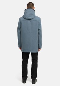 Kék kapucnis kabát sima textúrával, hosszú ujjak, egyenes fazon, fekete nadrággal és sötét lábbelivel párosítva.