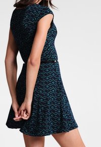 Granatowa sukienka w zygzakowaty wzór, krótkie rękawy, dopasowana góra i rozkloszowana spódnica. Teksturowana tkanina z geometrycznym wzorem.