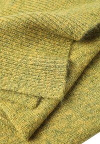 Tessuto spesso e a costine in un colore giallo-verde smorzato, con una consistenza morbida, fibre visibili e un aspetto stratificato.