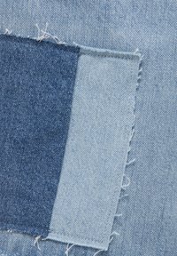 Échantillon de tissu en denim présentant deux teintes : indigo foncé et bleu clair. Les bords sont bruts avec des fils effilochés et des variations distinctes de texture.