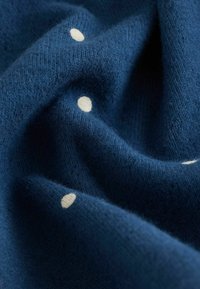 Marineblauwe gebreide stof met een zachte textuur, voorzien van verspreide witte stippen, die een gezellige uitstraling benadrukken en fijne stikdetails tonen.