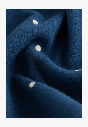 Morjeno modra pletenina z mehko teksturo, ki vsebuje razpršene bele pike, kar poudarja prijeten videz in zapleteno šivanje.