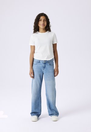 T-shirt blanc à manches courtes associé à un jean bleu clair à jambes larges. Le jean présente une poche avant et une fermeture à bouton, avec un lavage décoloré.