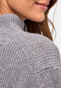 Maglione grigio a maglia con texture a coste e colletto alto, evidenziando dettagli di cucitura sulla spalla.