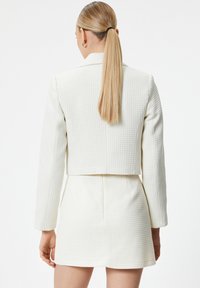 Witte, textuurvaste blazer met een cropped ontwerp en lange mouwen, gecombineerd met een bijpassende korte rok. Heeft een schone, op maat gemaakte silhouet.