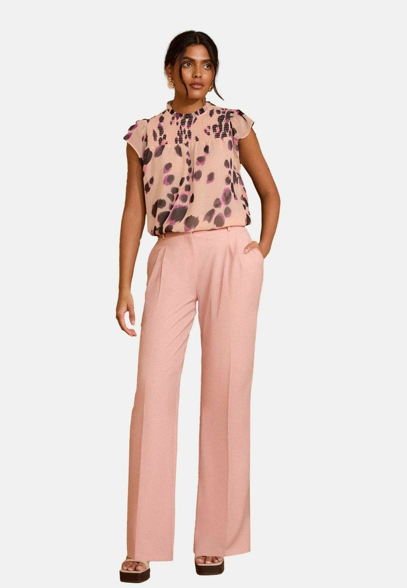 Blusa con mangas en forma de pétalo en suave color rosa y estampado abstracto en púrpura, combinada con pantalones de pierna ancha de tiro alto en rosa claro.