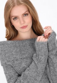 Szürke kötött pulóver széles, vállakat szabadon hagyó nyakkivágással, puha tapintással és bordázott mintázattal. Hosszú ujjak mandzsetta részletekkel. Tiszta varrás.