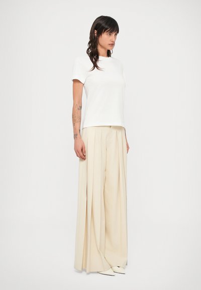Biele bavlnené tričko s krátkymi rukávmi v kombinácii s vysokým pásom, béžovými plisovanými nohavicami. Hladká textúra; minimalistický dizajn; priliehavý top, voľné nohavice.