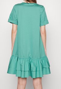 Robe teal avec des manches courtes à revers et un ourlet en volants empilés. Matière en coton doux, coupe décontractée, design simple sans motifs supplémentaires.