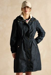 Tumši jūras zilas krāsas lietusmētelis ar rāvējslēdzēju un pogu iekšu, sašaurināmu jostu, divām sānu kabatām un kapuci. Audums ir ar nemanāmu ziedu rakstu.